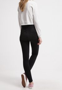Černé skinny džíny s vysokým pasem, doplněné o světle šedou zkrácenou mikinu a růžové nazouvací boty, které ukazují hladkou texturu.