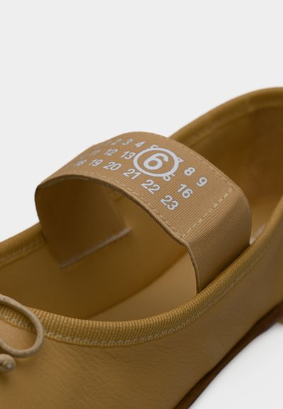 Καφέ δερμάτινο παπούτσι με υφασμάτινο ιμάντα πάνω από το άνοιγμα, που φέρει λευκούς αριθμούς και έναν αριθμό 6 σε κύκλο στο κέντρο.