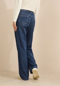 Jeans i mörkblå denim, lös passform med raka ben, med bakfickor och kontrastsöm. Parat med vita sneakers.