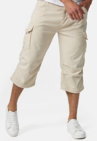 Pantalons cargo beiges avec une longueur au genou, dotés de poches latérales et d'une taille avec cordon de serrage. Tissu lisse avec une coupe décontractée et des coutures simples.
