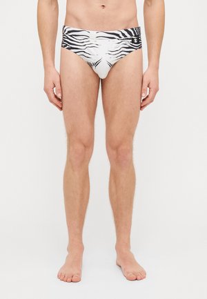 Weiße Schwimmwäsche mit einem schwarzen Zebra-Streifen-Muster, elastischem Bund und kleinem Logo-Detail auf der Vorderseite. Weicher, dehnbarer Stoff.