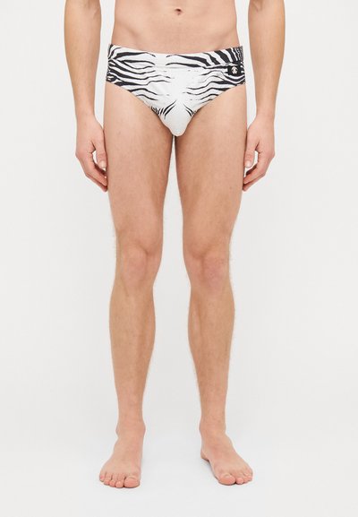 Bílé plavecké trenýrky s černým pruhovaným vzorem zebra, elastický pas a malý logo detail v přední části. Měkká, pružná látka.