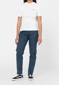 Vitt bomullslinne med korta ärmar och rund halsringning, kombinerat med mörkblå byxor. Svarta och vita sneakers har kontrasterande ränder.