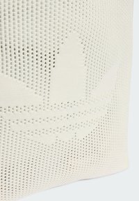 Pleteni bijeli platneni torba s perforiranim uzorkom koji uključuje suptilan logotip, glatkom teksturom i zaobljenim oblikom.