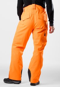 Oranje waterdichte broek met zwarte accenten, voorzien van verstelbare banden, twee achterzakken en een losse pasvorm voor gemakkelijke beweging.