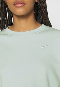 Mintgrön sweatshirt med rundad halsringning, med en liten silverfärgad Nike-logotyp på vänster bröst. Mjuk, strukturerad tyg.