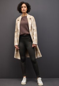 Beige ruuduline mantel pikkade varrukatega pruunist svetriga, koos mustade retuuside ja valgete tossudega. Sujuv kangas puhaste joontega.