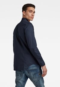 Camicia a maniche lunghe blu navy con colletto abbottonato, leggermente lucida e orlo curvo, abbinata a jeans azzurri chiari con un design sbiadito.