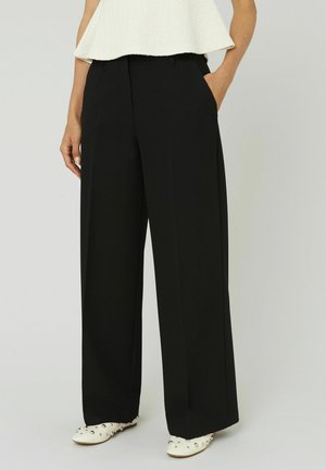 Pantalons larges noirs en tissu lisse ; dotés de poches latérales et d'une coupe ajustée, associés à un haut blanc texturé.