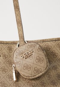 Beige tote bag with textured fabric featuring a subtle pattern. Includes a small detachable pouch with a gold logo and zipper.