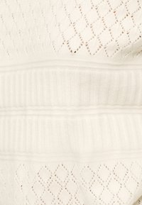 Λευκό πλεκτό ύφασμα με διαμάντι σχέδιο, διακοσμημένο με διακριτικές διαφάνειες και υφασμένο ριμπ υφή στη μέση. Ολοκληρωμένο με ομαλή υφή.