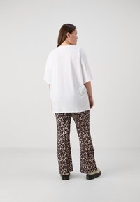 Bílý oversized tričko s krátkými rukávy, spárované s rozšířenými kalhotami s leopardím vzorem v hnědé a černé barvě. Černé chunky boty.