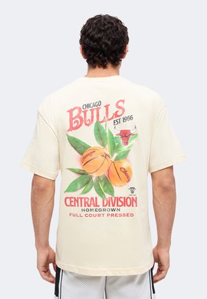 Άνδρας που φοράει ανοιχτό μπεζ μπλουζάκι Chicago Bulls με γραφικά από μπάσκετ και φύλλα και κείμενο στην πλάτη, στραμμένος με την πλάτη στην κάμερα.