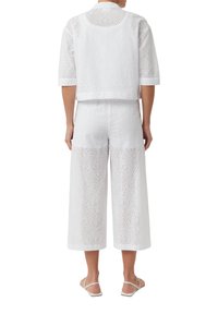 Weißes, gesticktes Baumwoll-Zweiteiler-Outfit mit einem verkürzten Oberteil mit kurzen Ärmeln und weitem Hosenbein, das mit floralen Ausschnitten verziert ist.