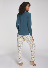 Bekväm tvådelad pyjamasuppsättning med en långärmad topp i teal och vita byxor med en färgglad blommönster. Mjuk tyg, avslappnad passform.