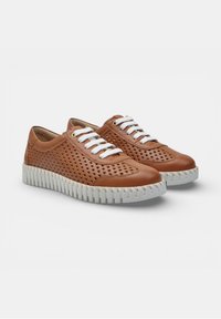 Zapatillas deportivas de cuero marrón con cordones blancos, lados perforados y suelas blancas gruesas ranuradas sobre un fondo blanco liso.