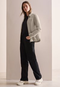 Chaqueta gris con cremallera y cuello, pantalones ajustados negros y zapatillas blancas. La chaqueta presenta una textura suave y bolsillos laterales.
