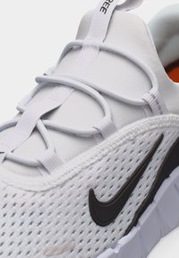 Baskets Nike blanches avec logo swoosh noir, tige en mesh respirant, lacets à boucle élastique et languette en tissu avec tirette.