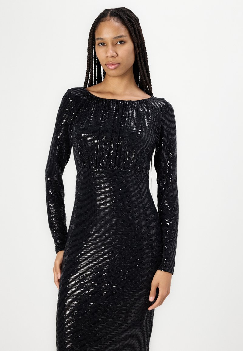 Czarna sukienka z cekinami, z długimi rękawami, dekoltem w łódkę, dopasowaną sylwetką i marszczonym detalem w okolicy biustu. Powierzchnia ma błyszczący, teksturowany wzór.