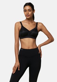 Czarny biustonosz o gładkiej fakturze, z szerokimi ramiączkami, dekoltem w kształcie litery V i wspierającym fiszbinem. Noszony z czarnymi legginsami z wysokim stanem.