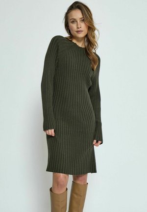 Dark green ribbed knit dress with long sleeves, crew neckline, and side slit detail, paired with knee-high tan boots.
