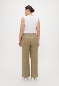 Ανοικ�τού πράσινου χρώματος παντελόνια με φαρδιά πόδια και υφή σε διαμαντένιο σχέδιο, συνδυασμένα με εφαρμοστό λευκό αμάνικο μπλουζάκι, με θέα από πίσω.