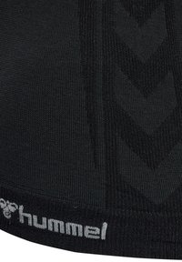 Schwarzes Sportoberteil mit strukturiertem Strickmuster. Verfügt über ein auffälliges Logo am Saum und ein Chevron-Design in einem leicht dunkleren Farbton.