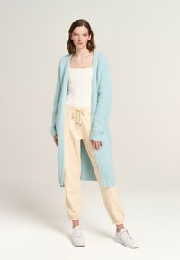 Light blue long cardigan made of textured knit fabric. Paired with cream joggers and white sneakers. Features open front and long sleeves.