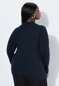 Marineblauwe lange mouwen trui met een hoge hals, geribbelde textuur en een relaxed fit, weergegeven vanuit de achterkant.