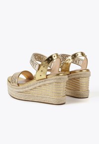 Zlatne wedge sandale s teksturiranim espadril podplatom, s križnim trakama i elastičnim trakama s logom. Sazvane akcentuacije na peti.