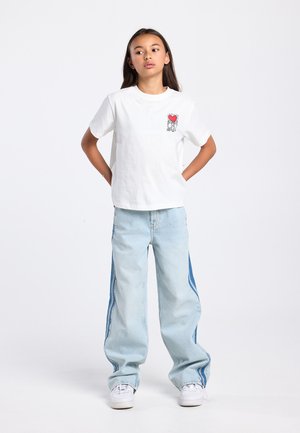 Wit katoenen T-shirt met een kleine rode afbeelding en zwarte omlijning op de linkerborst; lichtblauwe oversized spijkerbroek met contrasterende zijpanelen en witte sneakers.