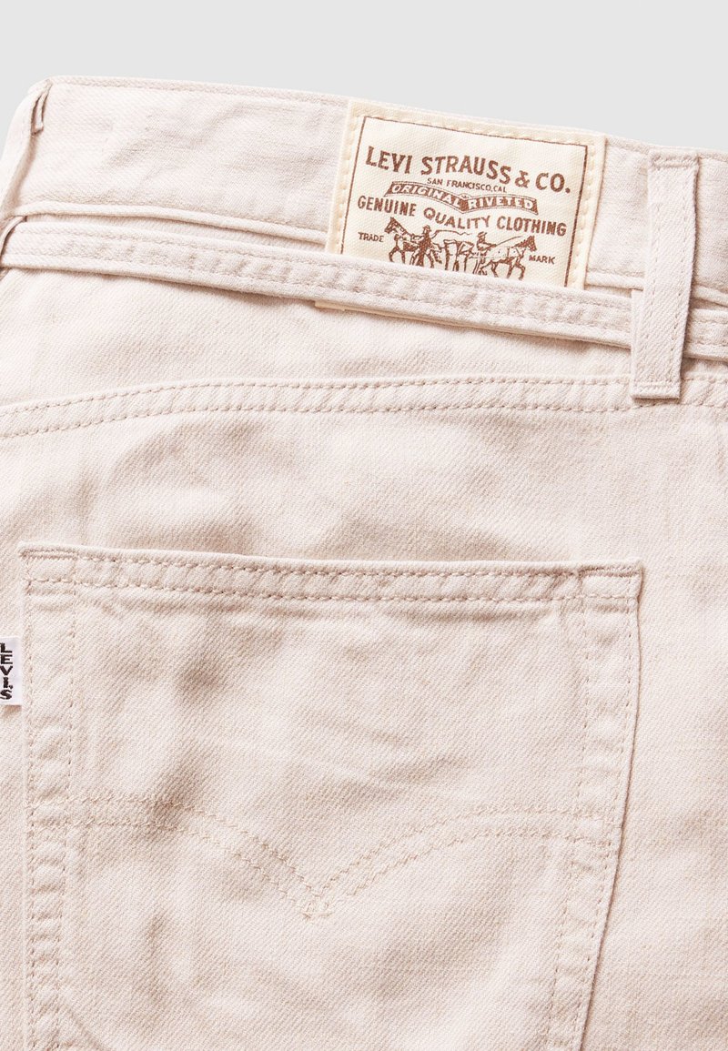 Jeans in denim beige con etichetta in pelle con "Levi Strauss & Co." e design distintivo della tasca posteriore. Texture liscia e cuciture standard.