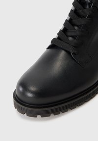 Bota de cuero negro con punta redondeada, superficie texturizada, cordones negros y una suela de goma rugosa y con patrón para un agarre mejorado.