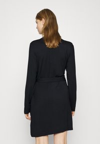 Svart langermet kjole med belte i midjen, har et enkelt design og glatt tekstur, faller over kneet.