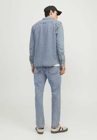 Svetlo modra denim jakna z gumbnim zapiranjem spredaj, dolgimi rokavi in dvema žepoma na prsih; v kompletu s svetlo modrimi kavbojkami in bež čevlji.