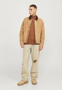 Beige katoenen jas met een bruine corduroy kraag, bruine coltrui, licht gerafelde jeans en beige laarzen. Eenvoudige snit, casual pasvorm.