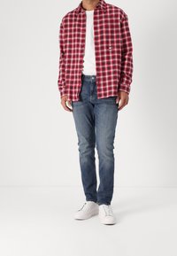 Koszula flanelowa w czerwono-czarną kratę na białej koszulce, niebieskie dżinsy i białe trampki. Ogólnie casualowy strój o luźnym kroju.