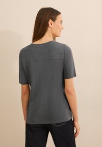 T-shirt grigia a maniche corte realizzata in tessuto leggero, con scollatura rotonda e dettaglio di cucitura orizzontale sulla schiena.