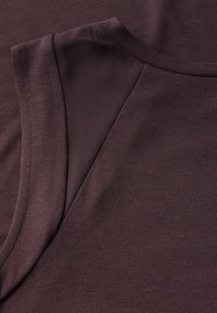 Bordowy top bez rękawów wykonany z dzianiny, prezentujący gładką teksturę z detalem szwu na ramieniu, minimalistyczny design.