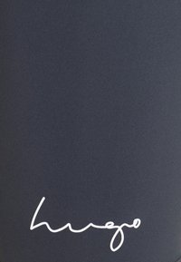 Námořnické sportovní legíny vyrobené z texturované látky s bílým kurzivním logem na dolní části nohy. Jednoduchý, elegantní design.