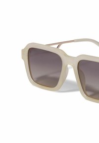 Gafas de sol con montura cuadrada de gran tamaño en color crema, lentes ahumados y finos detalles metálicos. Presenta una textura brillante.