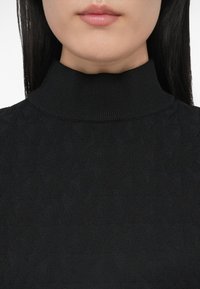 Must turtleneck kampsun tekstuurse mustriga, soonikkoes kaelus ja pehme kangas. Lähedalt vaadatuna, fookusega kraele ja ülemisele rinnapiirkonnale.