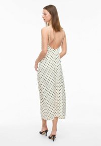 Robe mi-longue noire à pois blancs avec un décolleté dans le dos, des fines bretelles et un tissu fluide, associée à des chaussures à talons hauts noires.