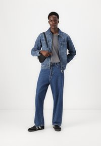 Denim jacket with faded blue color and front pockets, gray t-shirt, wide-leg blue jeans, and black sneakers with white stripes.