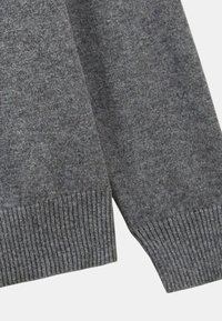 Détail d'un pull en tricot gris montrant des poignets et un ourlet côtelés, une texture lisse, et un mélange de fils clairs et foncés pour créer de la profondeur.