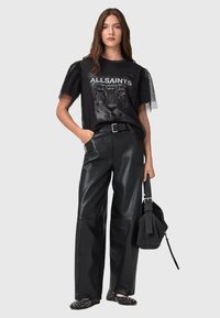 Top in rete nero trasparente con stampa leopardata e testo "ALLSAINTS", abbinato a pantaloni in pelle nera a vita alta e scarpe basse con motivo.