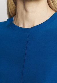 Niebieski sweter z okrągłym dekoltem i widocznymi szwami wzdłuż szwu. Gładka tekstura i dopasowany krój.