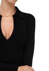 Top lungo a maniche ribattute nere con scollatura a V profonda, caratterizzato da un accento in metallo dorato al colletto. Tessuto morbido e design aderente.