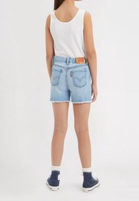 Wyblakłe, jasnoniebieskie szorty dżinsowe z postrzępionym obszyciem, wyposażone w tylne kieszenie i skórzaną naszywkę z logo na pasku. Noszone z białym topem na ramiączkach.
