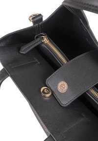 Sac à main en cuir noir avec une poche zippée et un fermoir à pression, présentant des éléments en or et une texture lisse. L'intérieur est spacieux et non doublé.